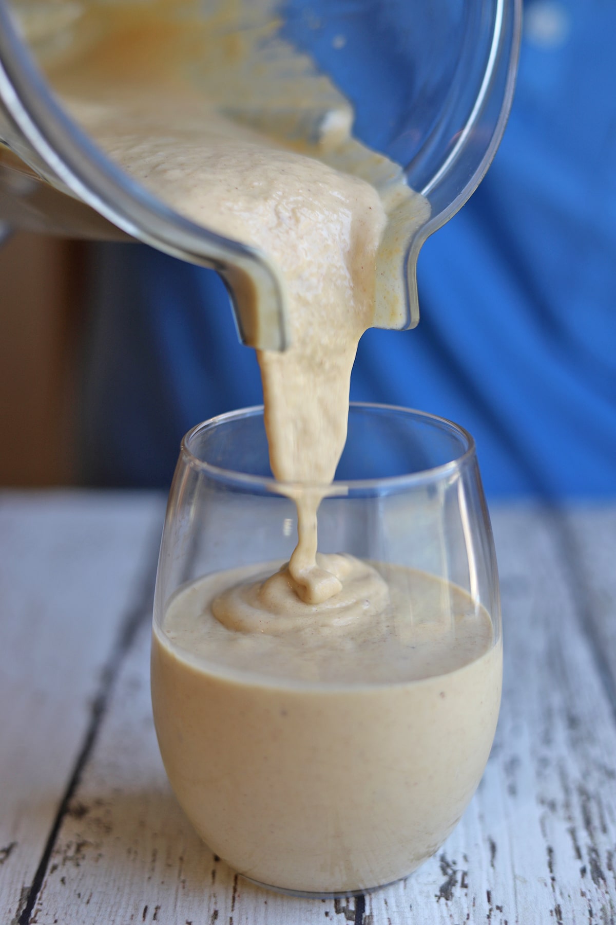 Peanut butter banana smoothie pouring from blender pitcher into glass.