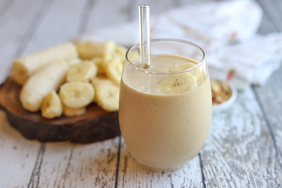 Peanut butter banana smoothie in glass by fresh banana chunks.