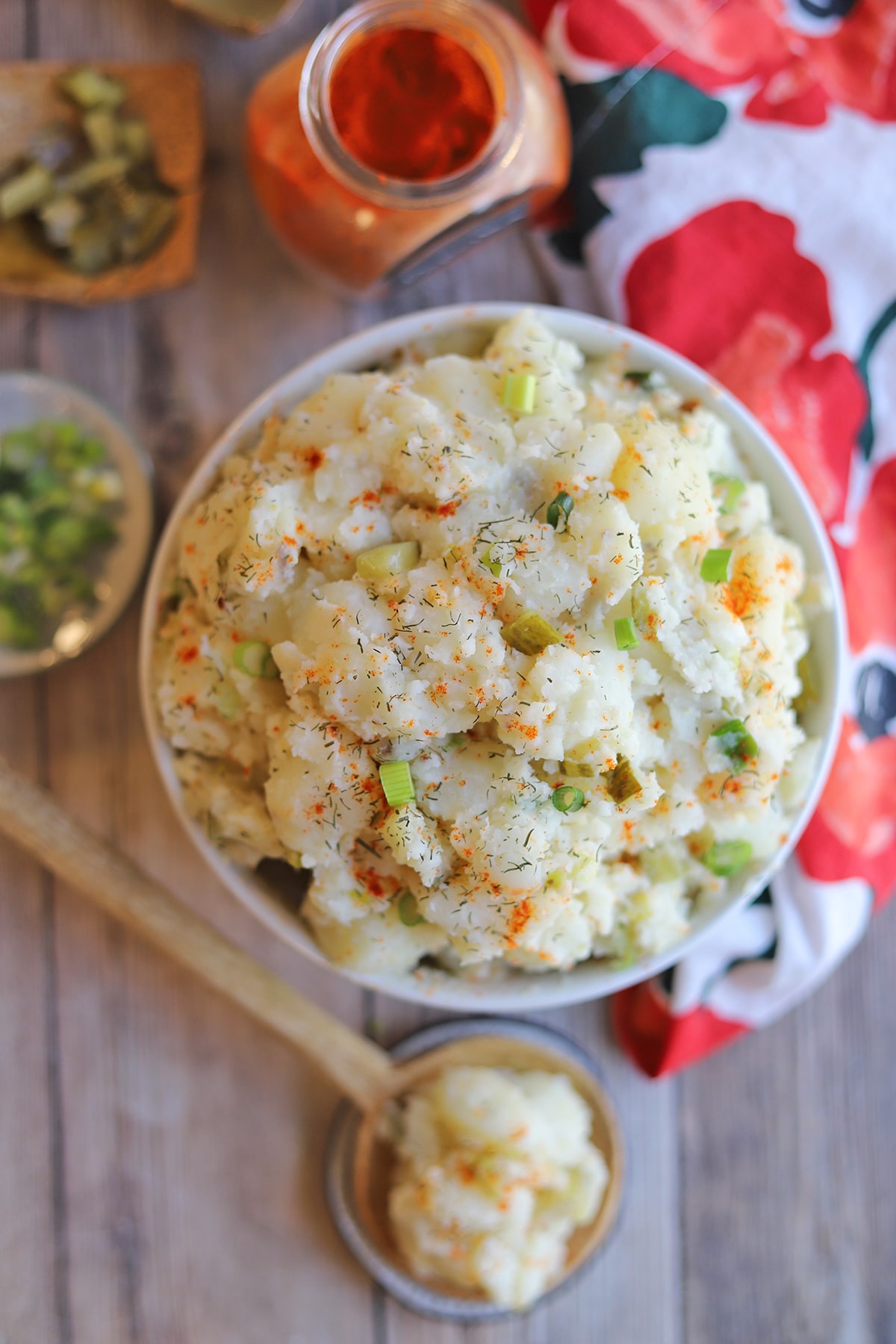 Overhead bowl of potato salad, paprika, green onions, and dill pickle pieces.