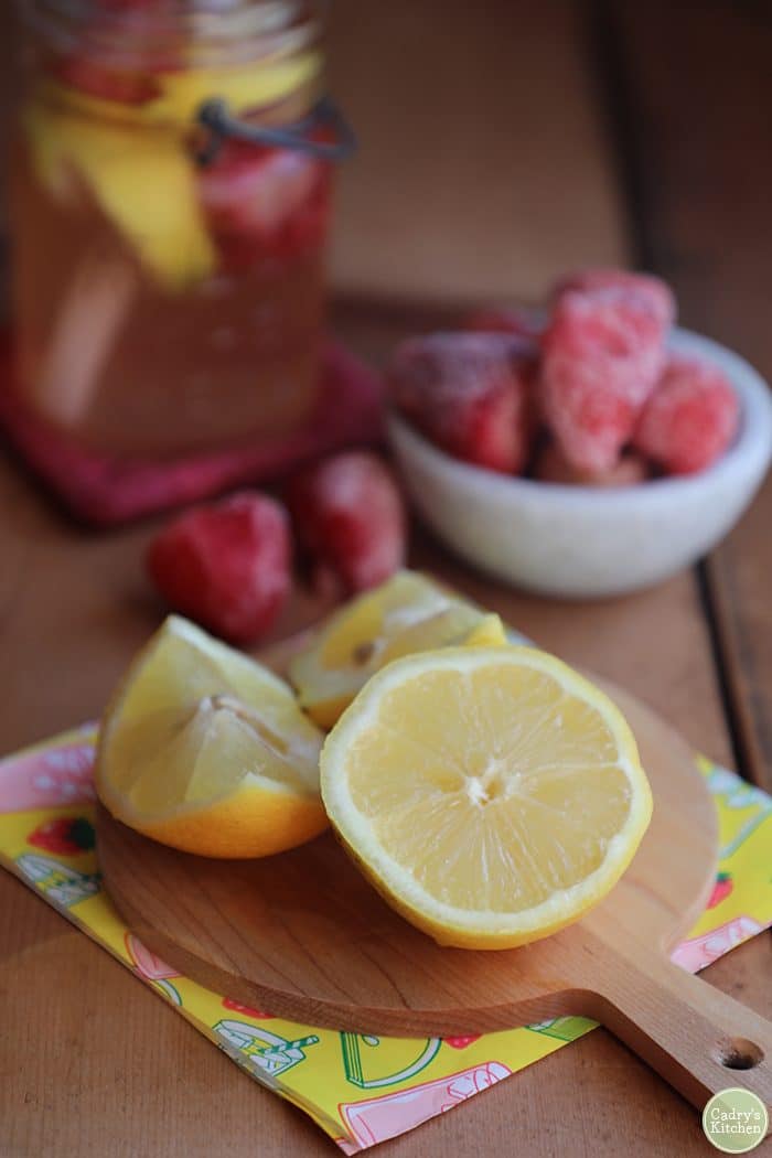 Cut lemon on a cutting board with frozen strawberries and sparkling strawberry lemonade.