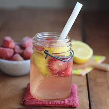 Sparkling strawberry lemonade in an Atlas jar with white straw. Frozen strawberries and cut lemons in background.