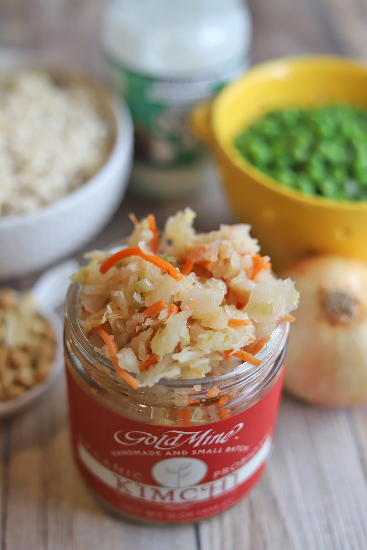 Jar of kimchi on table by peas, rice, and onion.