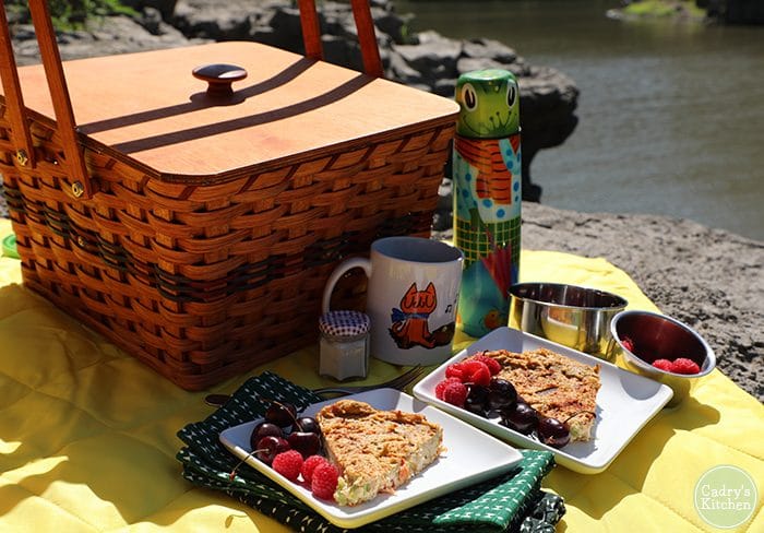 Vegan breakfast picnic with basket, thermos, coffee mug, and plates of quiche with berries.