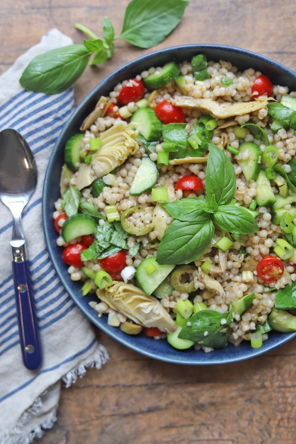 Israeli couscous salad in blue bowl by spoon.