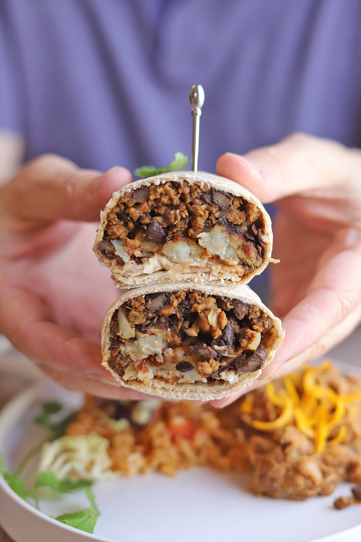 Hands holding burritos cut in half, showing tots & taco meat.