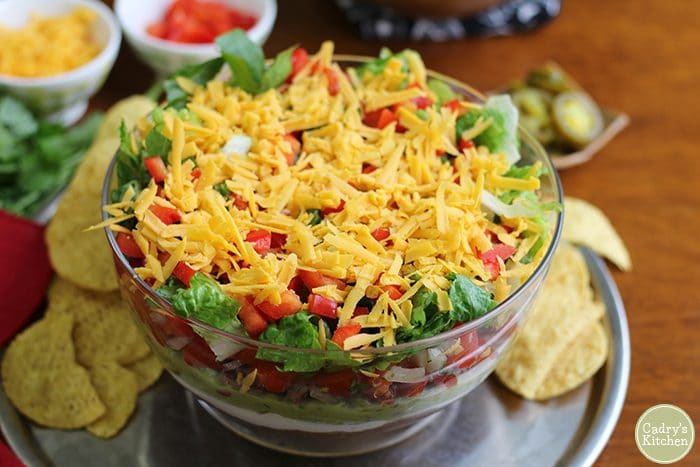 Overhead vegan 7 layer dip in glass bowl with corn tortilla chips.