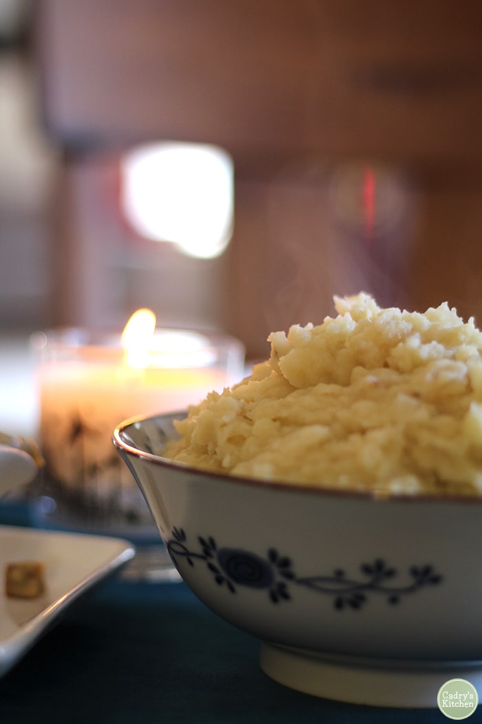 Bowl of mashed potatoes with candle in background.