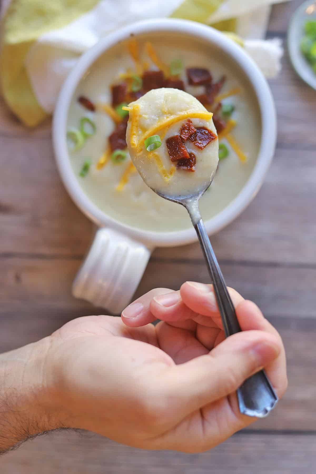 Spoonful of vegan potato soup with seitan bacon, vegan cheese, and green onions.
