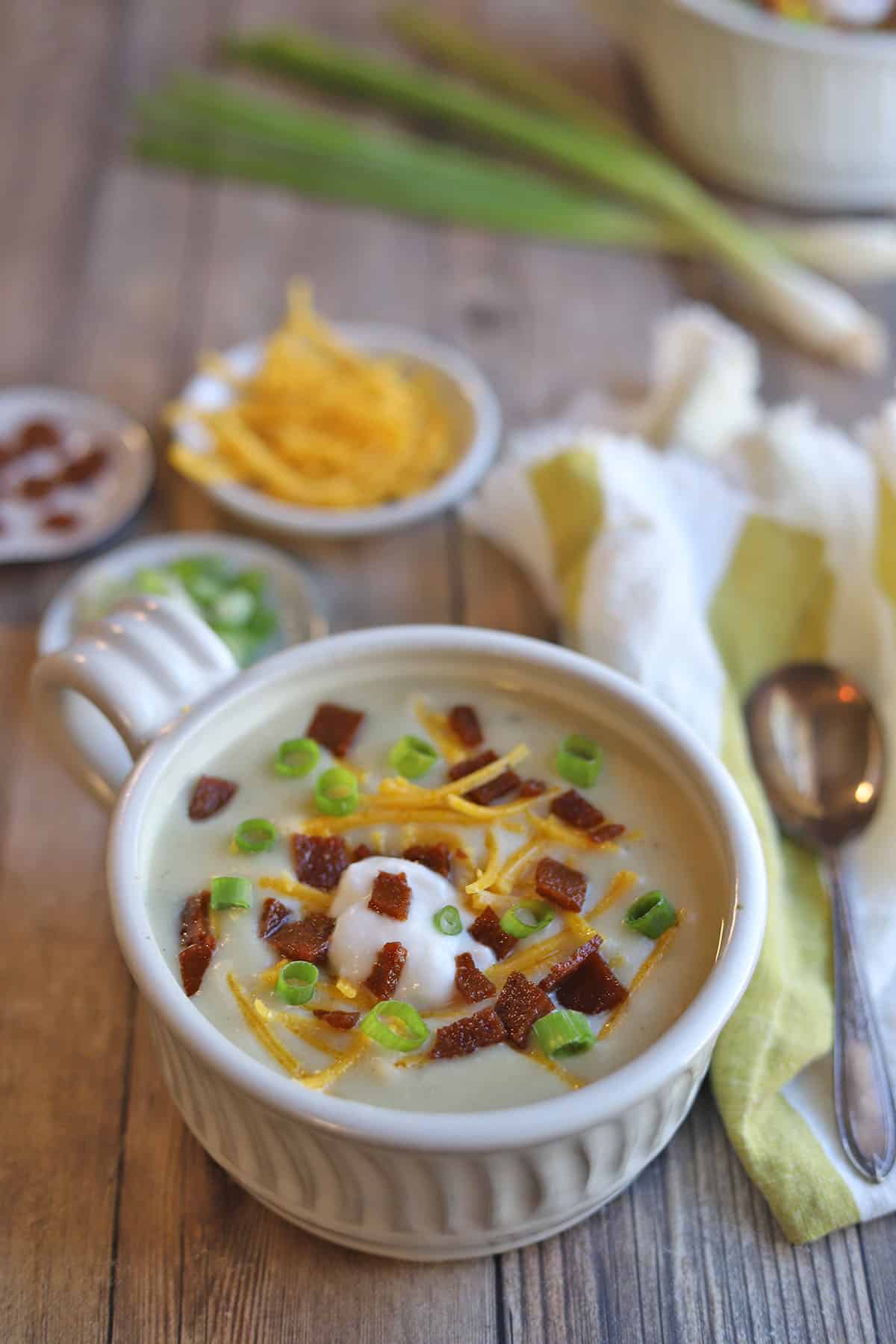 Vegan baked potato soup in bowl by toppings.