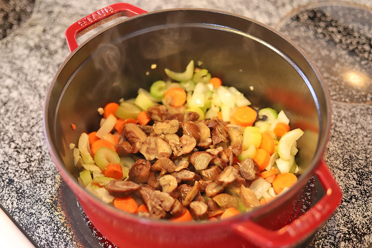 Staub pot on stove with chestnuts, onions, garlic, celery, and carrots.