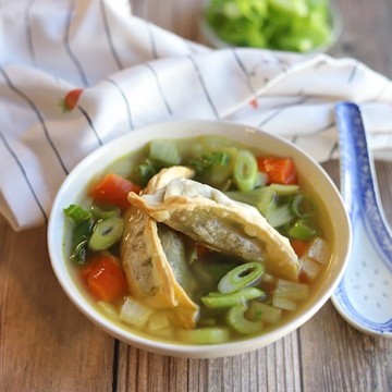 Vegetable potsticker soup in bowl by spoon.