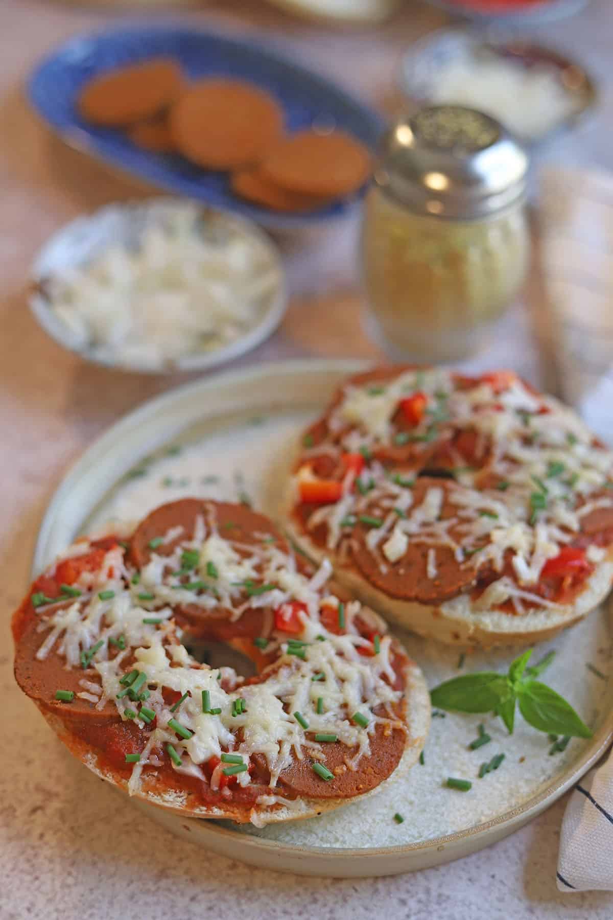 Air fryer pizza bagels on plate by parmesan cheese shaker.