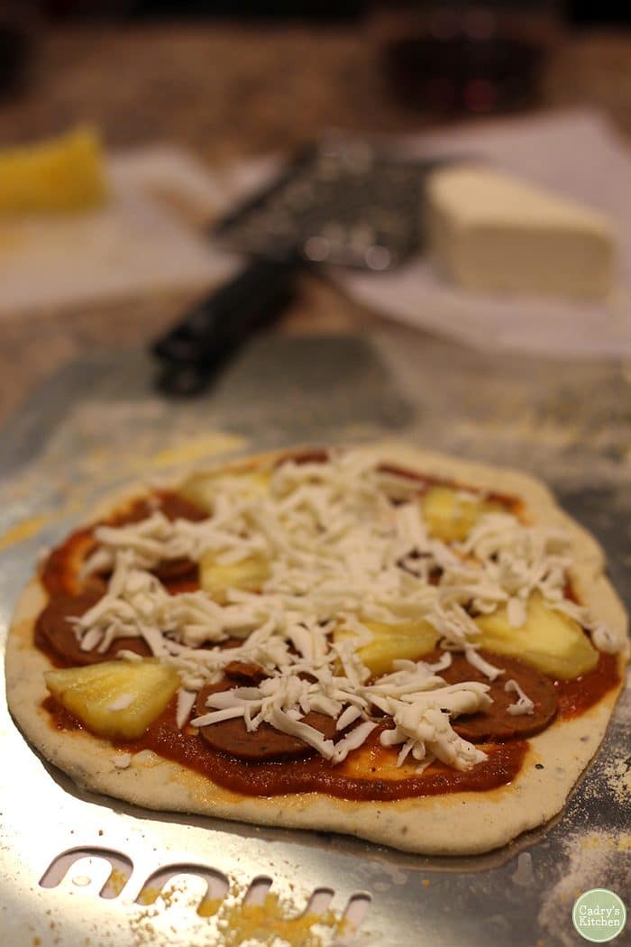 Vegan pizza with shredded Herbivorous Butcher mozzarella cheese, vegan pepperoni, and pineapple on pan.