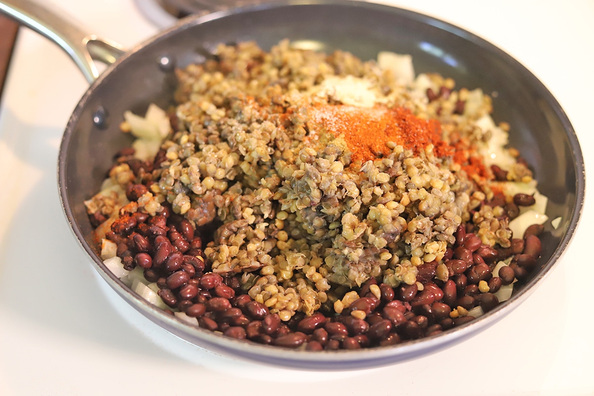 Spices on lentils and black beans in skillet.