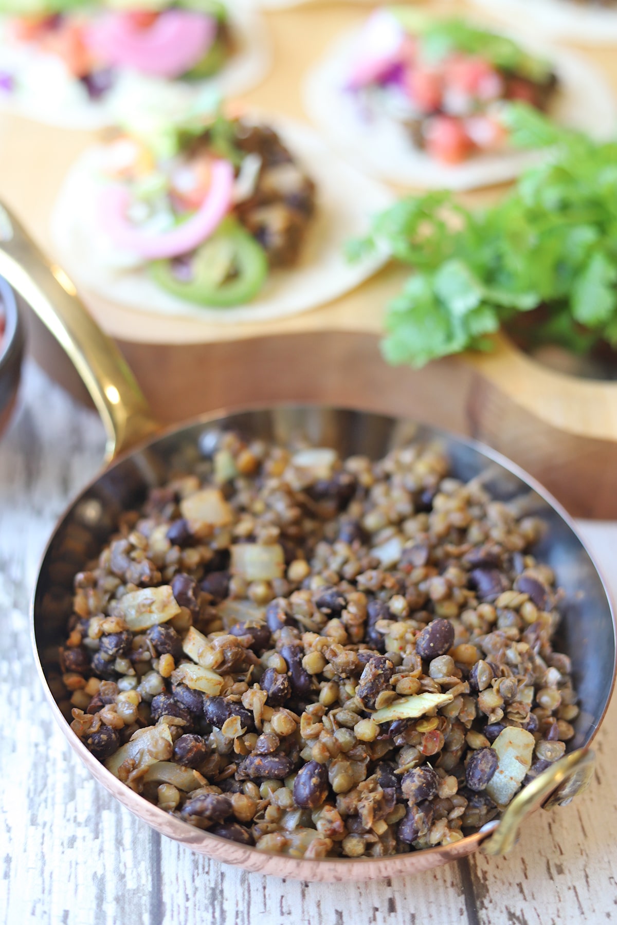 Lentil taco meat in pan by platter of tacos.