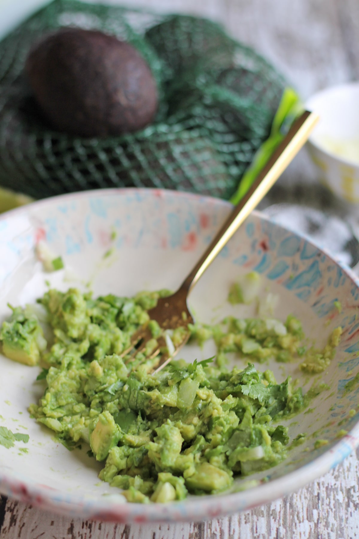 Avocado being smashed in bowl with garlic and cilantro.