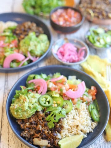 Vegan burrito bowl on table with pickled onions, and pico de gallo.