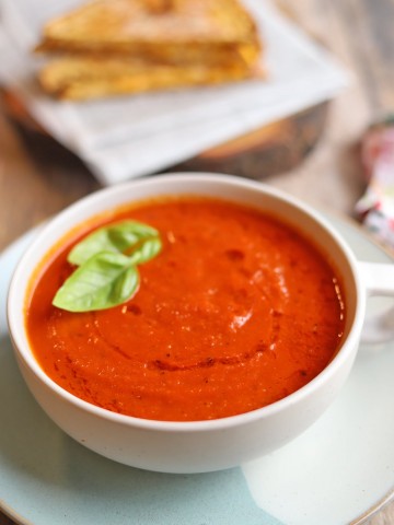 Bowl of vegan tomato soup with fresh basil by sandwich.