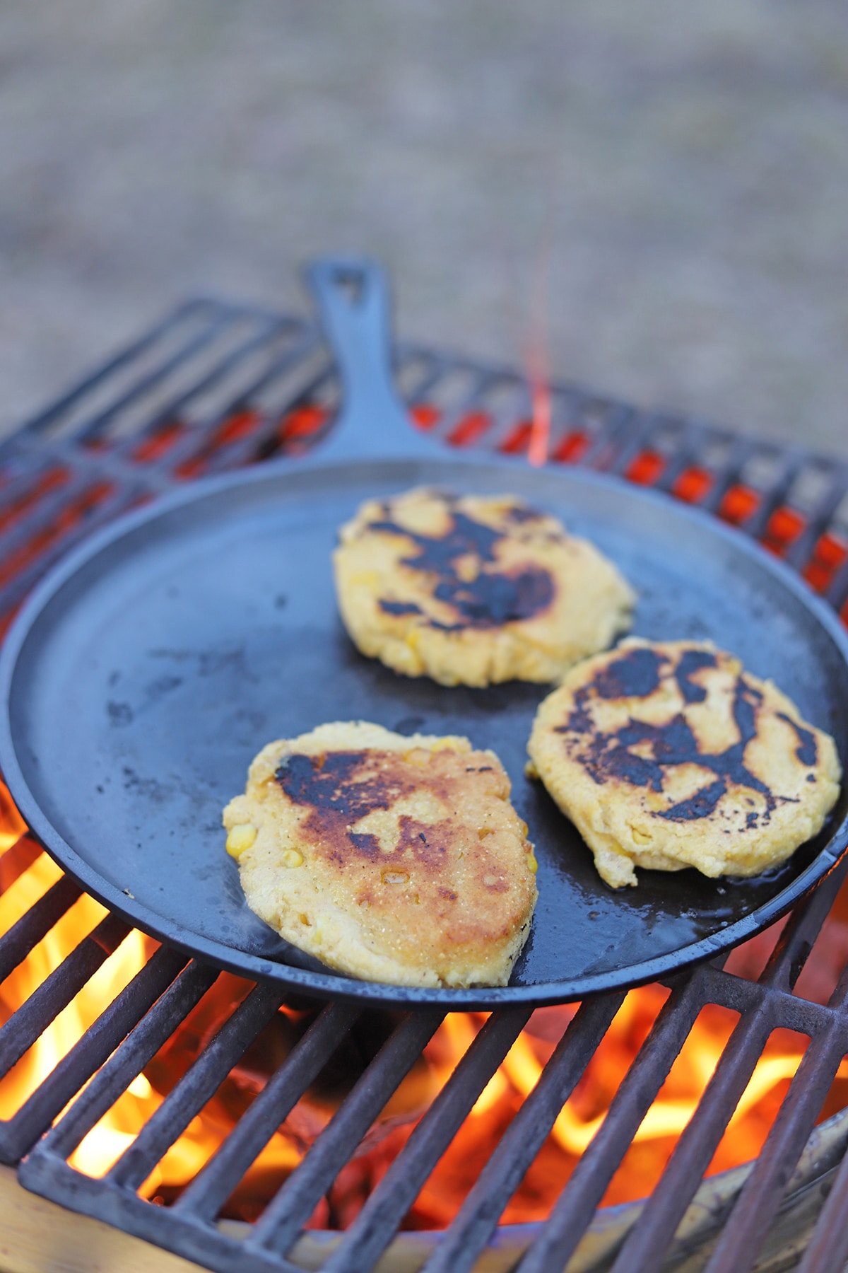 Pupusas cooking on a cast iron pan on a campfire.