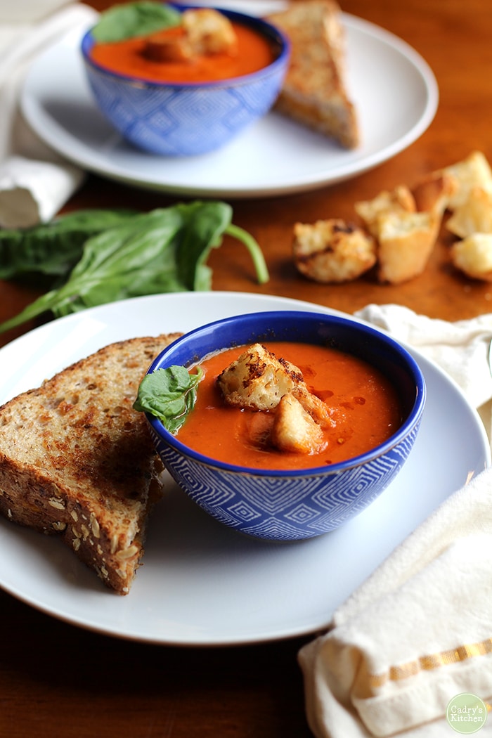 Creamy vegan tomato soup in blue bowl with half of a grilled cheese sandwich.