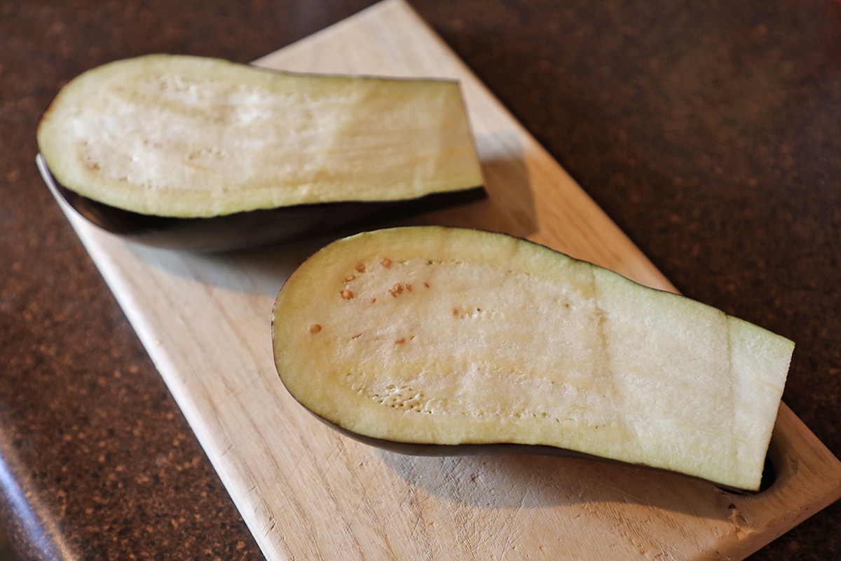 Eggplant sliced in half on cutting board.