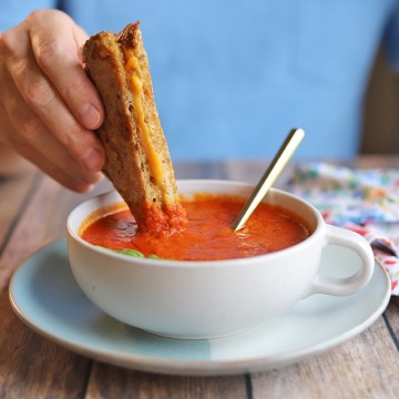 Grilled cheese being dipped into bowl of vegan tomato soup.