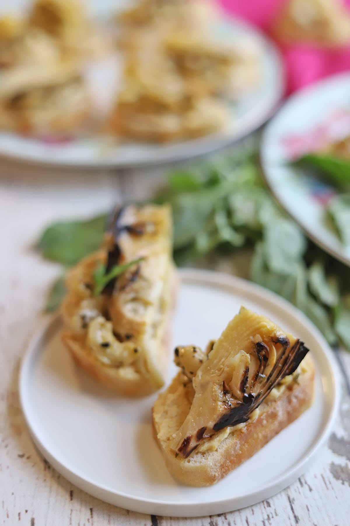 Toasted bread on plate with hummus, artichokes, and marinated cashews.