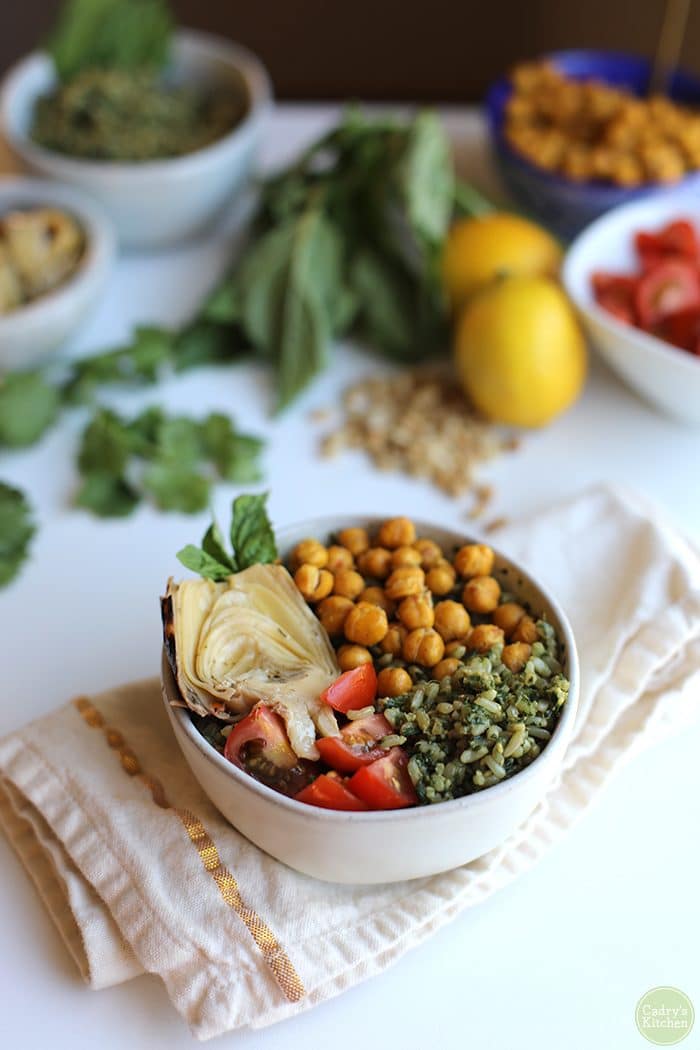 Vegan pesto rice bowl with grilled artichoke heart, cherry tomatoes, and roasted chickpeas on napkin.