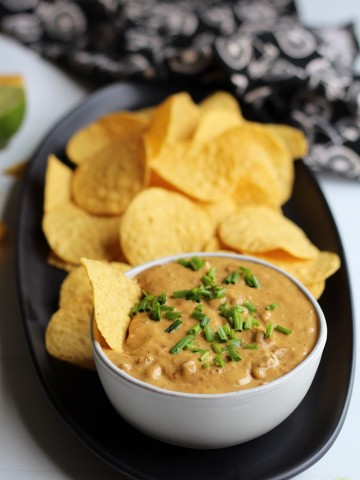 Vegan cheese dip in bowl with chives on top, tortilla chips, and napkin.