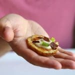 Hand holding loaded potato slice with cashew cream & seitan bacon.