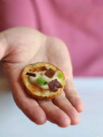 Hand holding sliced potato topped with cashew cream & seitan bacon