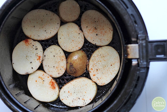 Sliced potatoes in air fryer basket.