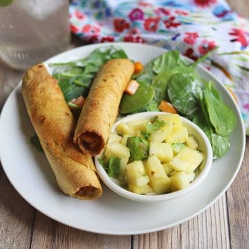 Two taquitos on plate with salad and pineapple salsa.