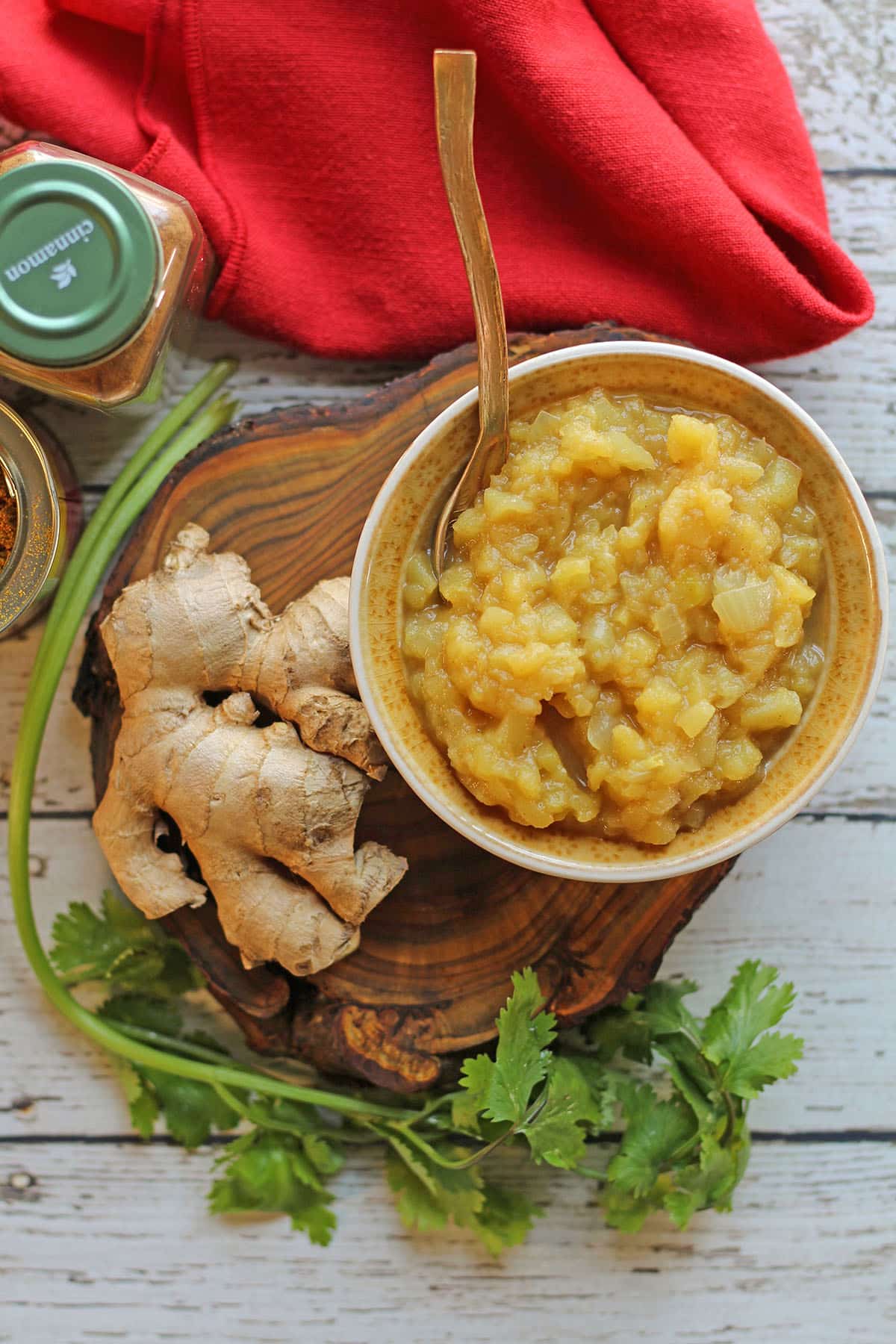 Apple chutney in a yellow bowl by cilantro, cinnamon, and ginger.