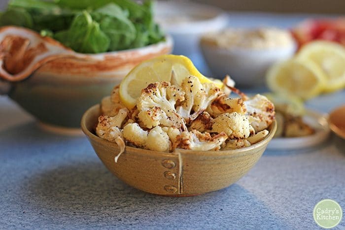Roasted cauliflower cooked in yellow bowl with lemon slice.