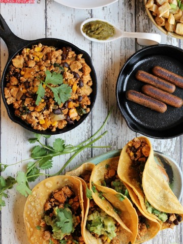 Overhead breakfast tacos on plate, Field Roast breakfast sausage in pan, and tofu scramble in skillet.