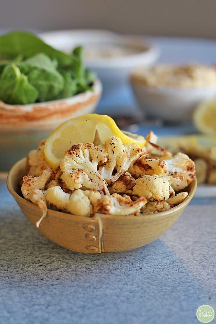 Close up roasted cauliflower in small bowl with lemon slice.