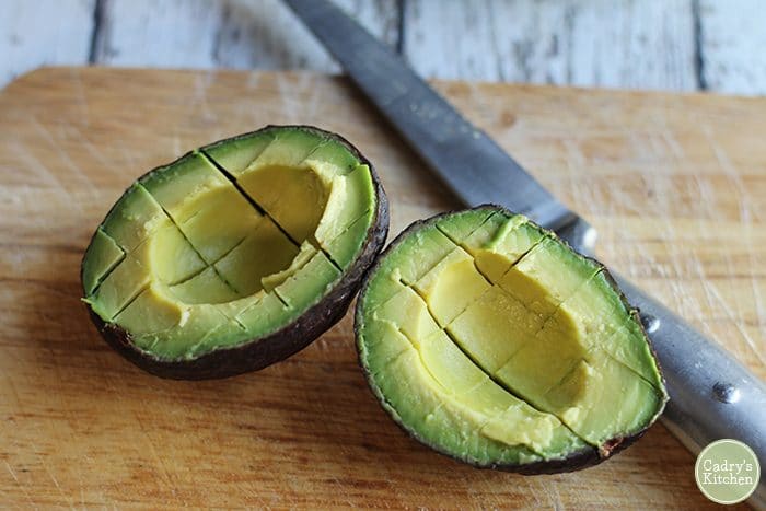 Scored avocado in peel with knife.