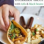 Text: Vegan breakfast tacos with tofu & black beans. Hand holding breakfast taco on plate with potatoes and veggie sausage.