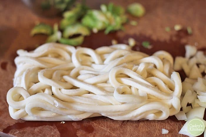 Unwrapped frozen udon noodles on cutting board.