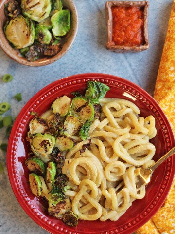 Overhead cheesy udon noodle bowl with Brussels sprouts & sriracha.