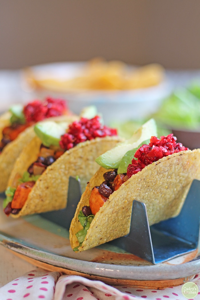 Sweet potato black bean tacos in taco holders, topped with cranberry salsa and avocado.