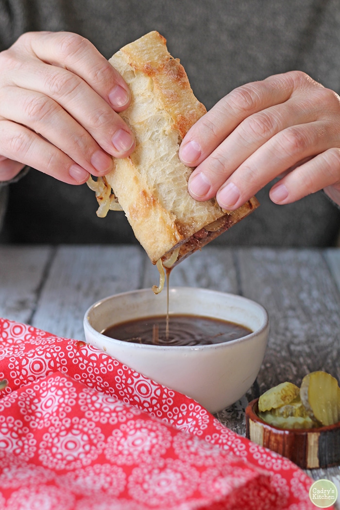 Hands dipping vegan French dip sandwich into au jus.