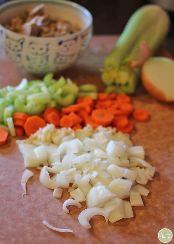 Vegan pot pie ingredients on cutting board - onions, garlic, carrots, and celery.