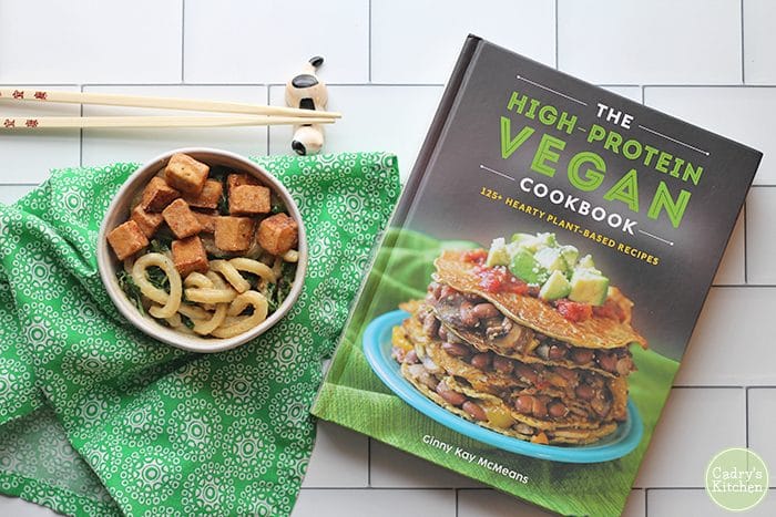 Overhead bowl of udon tossed in peanut sauce, spinach, and fried tofu cubes. High Protein-Vegan Cookbook by Ginny Kay McMeans.