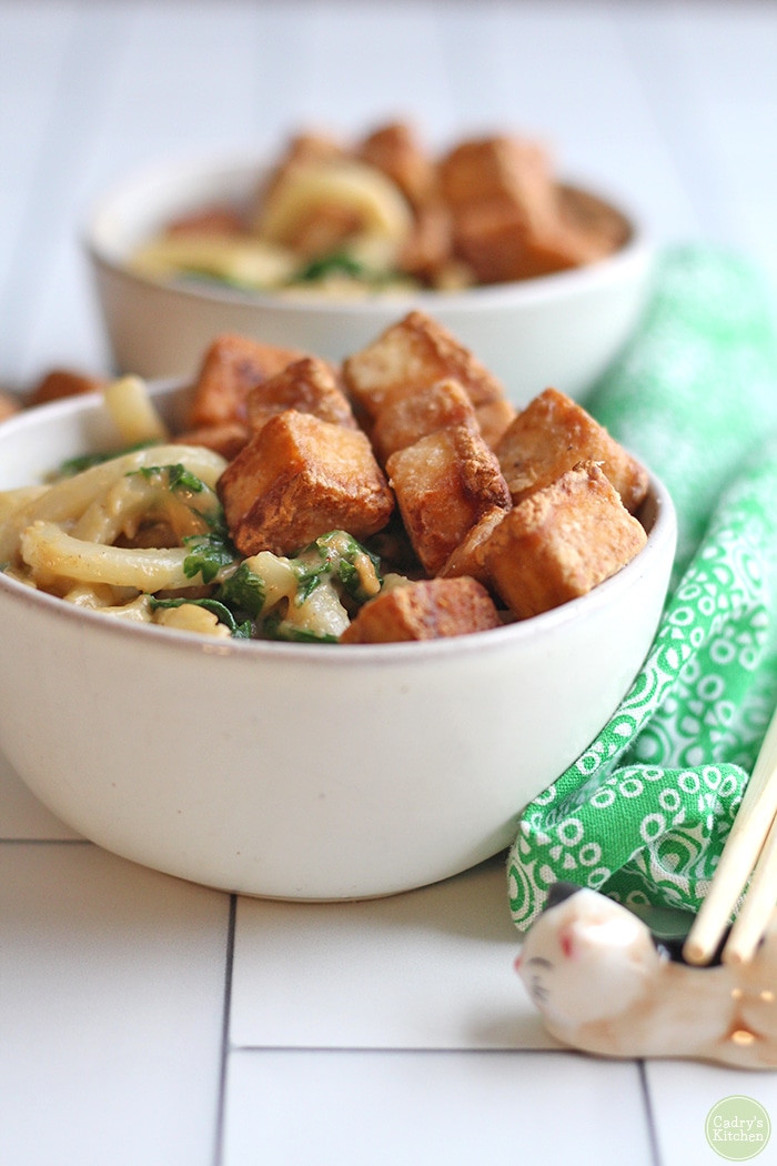 Bowl of peanut butter noodles with spinach, topped with fried hoisin tofu.