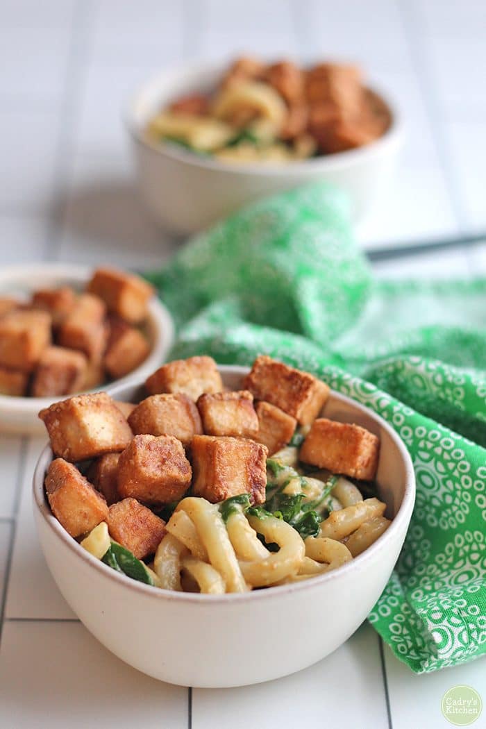 Bowl of udon noodles, topped with fried hoisin tofu & sauteed spinach by green napkin.