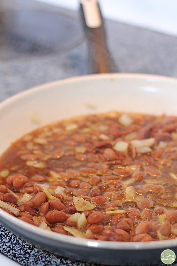 Pinto beans with onions, garlic, spices, and water in skillet for vegan refried beans.