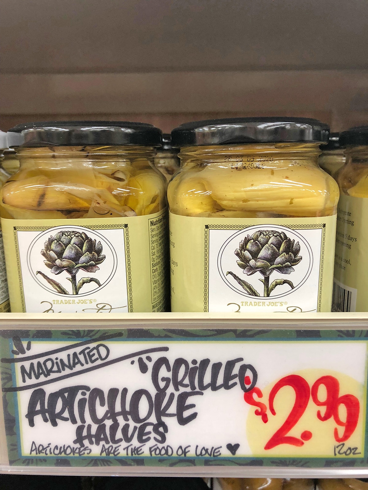 Jars of grilled artichoke halves on shelf.