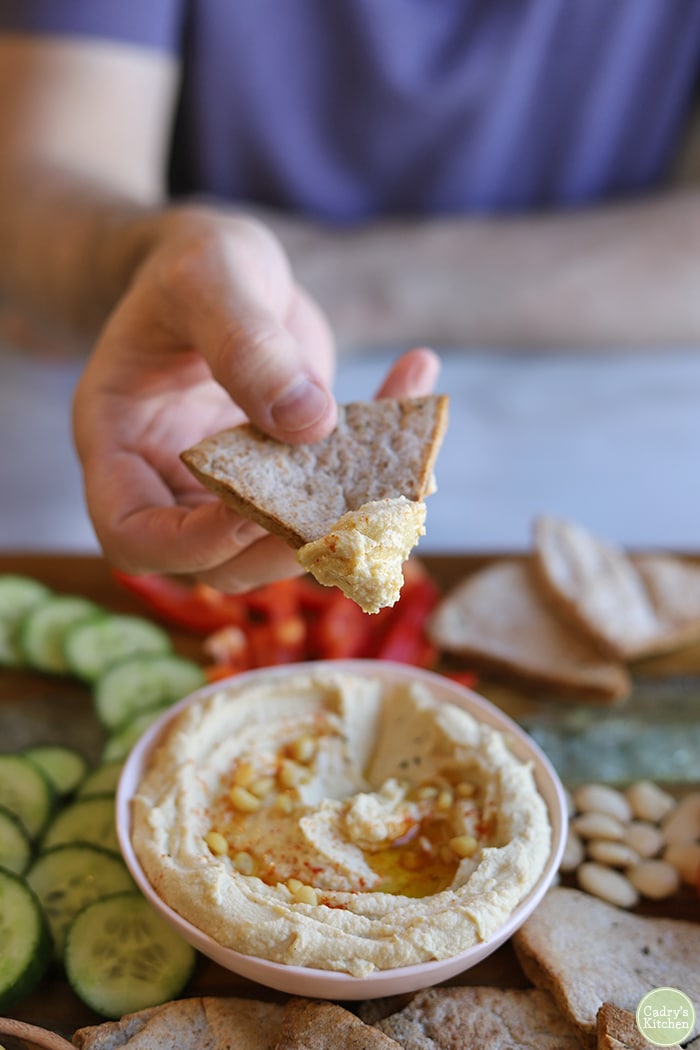 Hand dipping chip into bowl of hummus.